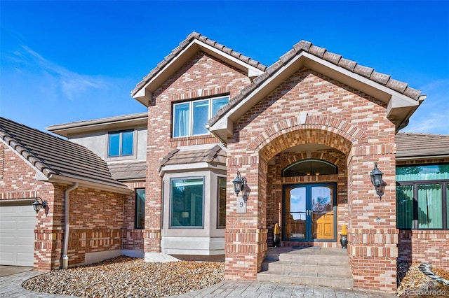 view of front of house featuring french doors, a tile roof, brick siding, and an attached garage