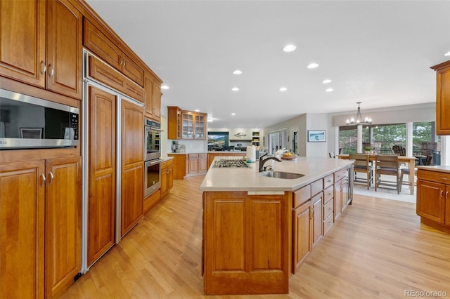 kitchen featuring brown cabinetry, a kitchen island with sink, a sink, and built in appliances