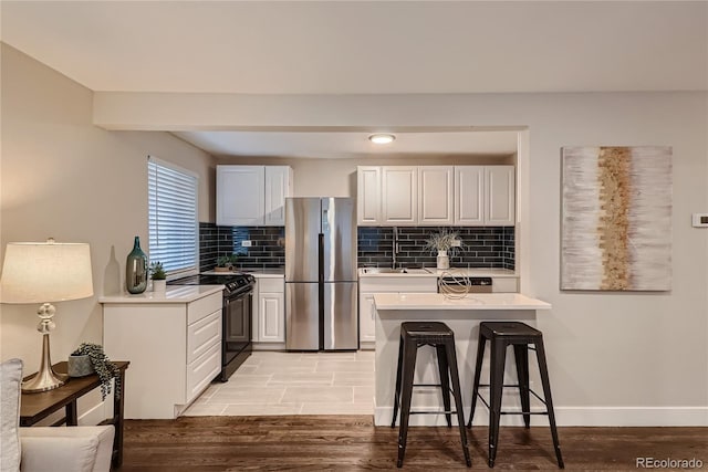 kitchen featuring stainless steel refrigerator, white cabinets, a breakfast bar area, electric range, and light hardwood / wood-style flooring