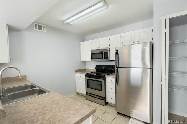 kitchen with light tile patterned floors, stainless steel appliances, white cabinetry, and sink