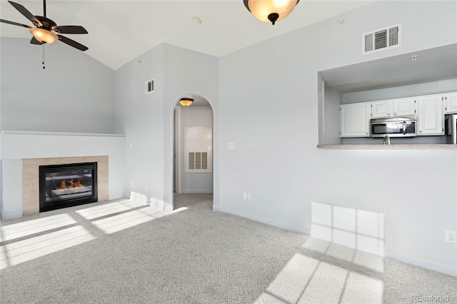 unfurnished living room with light colored carpet, high vaulted ceiling, ceiling fan, and a tiled fireplace