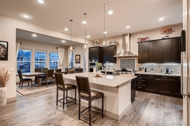 kitchen with wall chimney range hood, a kitchen bar, a sink, and tasteful backsplash