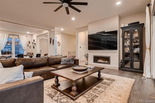 living area featuring a ceiling fan, recessed lighting, a warm lit fireplace, and hardwood / wood-style floors