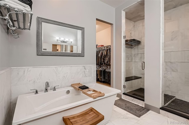 bathroom with a stall shower, marble finish floor, a walk in closet, a freestanding bath, and tile walls