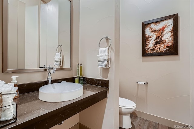 half bathroom with vanity, wood finished floors, and toilet