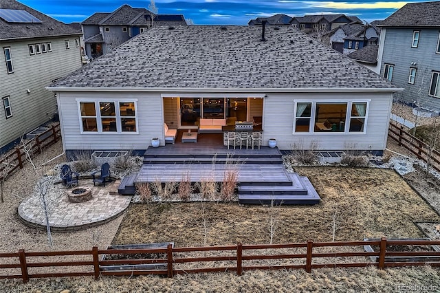 rear view of house featuring a deck, roof with shingles, a fire pit, and a fenced backyard