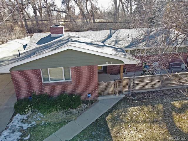 view of side of home featuring brick siding, roof with shingles, and a chimney