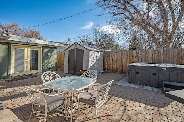 view of patio with an outbuilding, outdoor dining area, a hot tub, french doors, and a storage shed