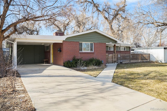 view of front of home featuring brick siding, concrete driveway, a front yard, a chimney, and a carport