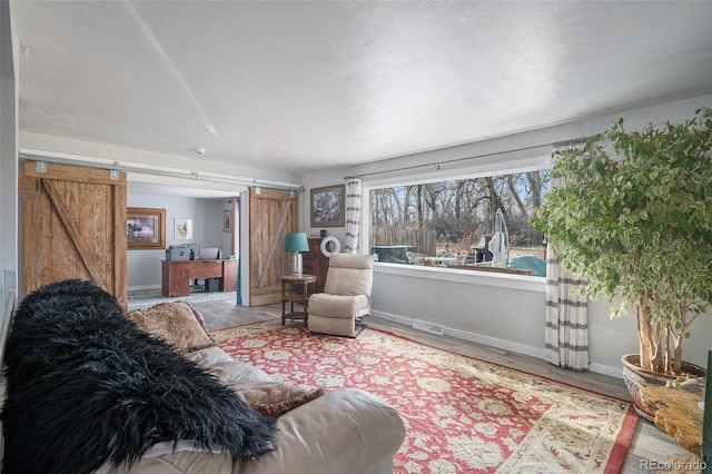 living room with a barn door, wood finished floors, baseboards, and visible vents