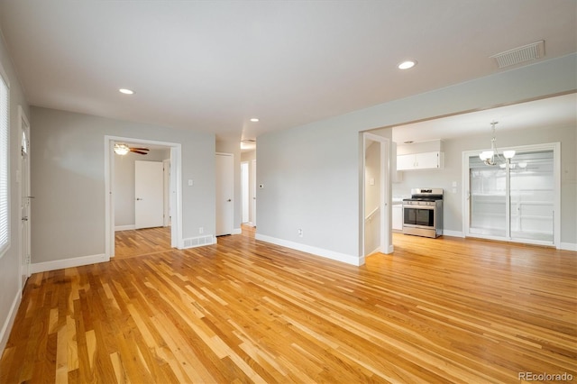 unfurnished living room featuring ceiling fan with notable chandelier and light hardwood / wood-style flooring