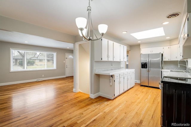 kitchen with decorative light fixtures, white cabinetry, stainless steel fridge with ice dispenser, and a skylight