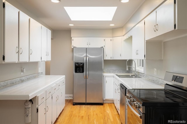 kitchen featuring white cabinets, sink, a skylight, light wood-type flooring, and appliances with stainless steel finishes