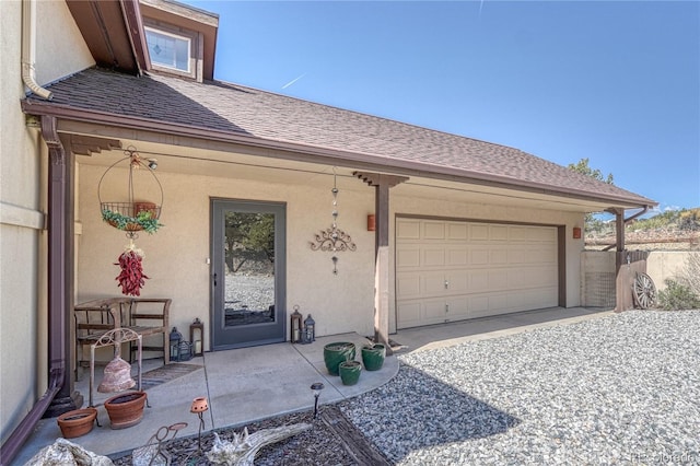 doorway to property featuring an attached garage, fence, a shingled roof, and stucco siding