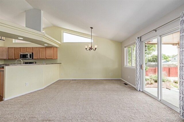 903 Cameron Dr, Severance, CO 80550 - kitchen with stainless steel microwave, vaulted ceiling, a chandelier, light colored carpet, and brown cabinets