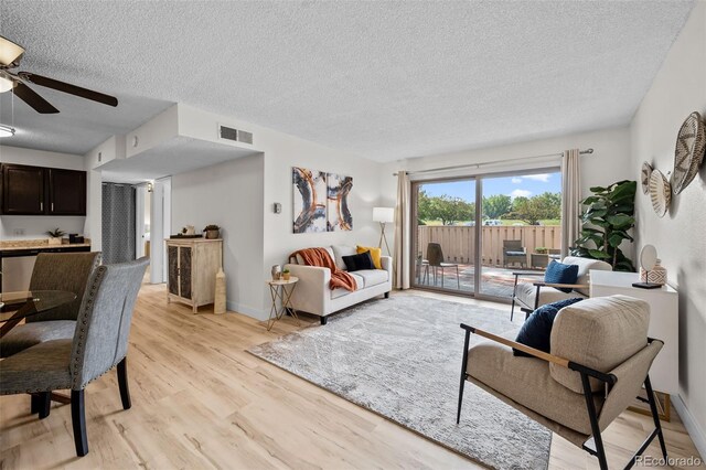 living room with a textured ceiling, ceiling fan, and light hardwood / wood-style floors