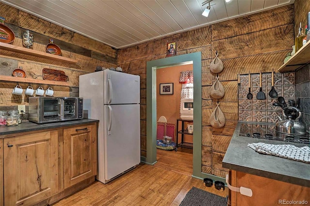 kitchen featuring light wood-type flooring, wood walls, black electric cooktop, and white refrigerator