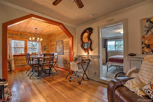 dining room featuring wood ceiling, ceiling fan with notable chandelier, wood walls, ornamental molding, and hardwood / wood-style floors