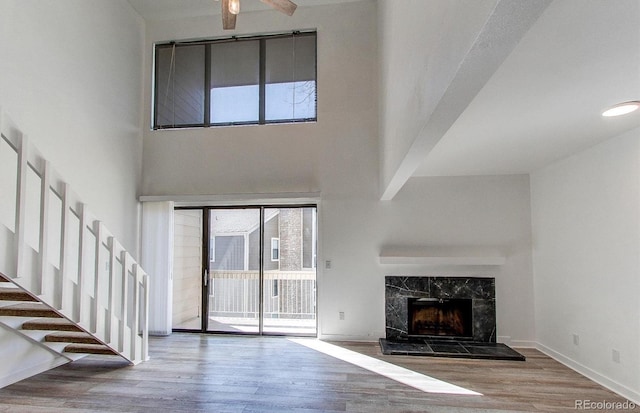 unfurnished living room with a towering ceiling, stairway, a high end fireplace, wood finished floors, and baseboards