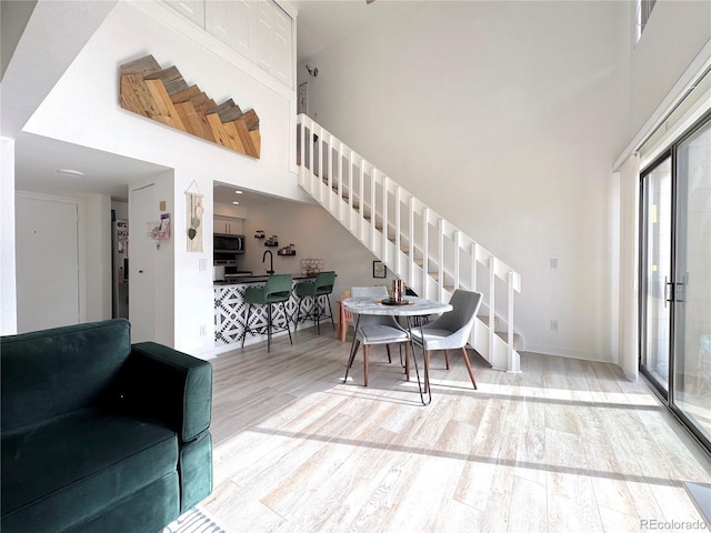 dining space featuring wood finished floors, a towering ceiling, baseboards, and stairs