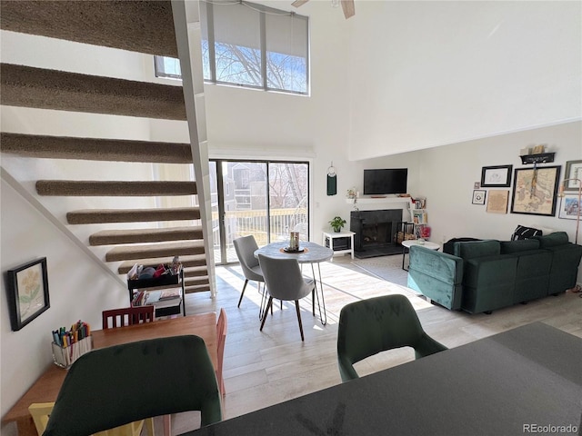 living room with light wood finished floors, a fireplace with raised hearth, ceiling fan, stairs, and a high ceiling