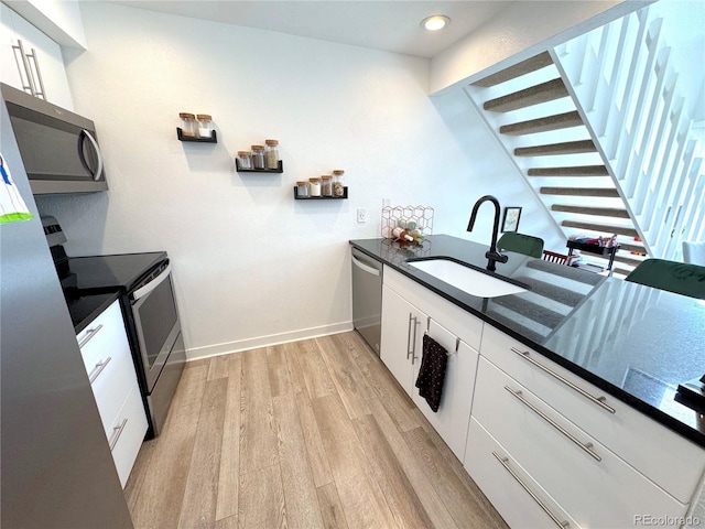 kitchen with a sink, baseboards, white cabinets, appliances with stainless steel finishes, and light wood-type flooring