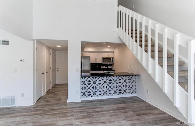 kitchen featuring stainless steel appliances, dark countertops, visible vents, and wood finished floors