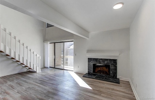 unfurnished living room featuring stairs, baseboards, a premium fireplace, and wood finished floors