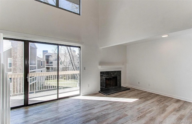 unfurnished living room featuring wood finished floors, a towering ceiling, baseboards, and a premium fireplace