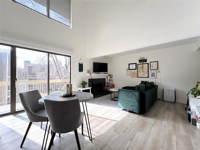 dining room featuring a fireplace with raised hearth, light wood finished floors, and a high ceiling