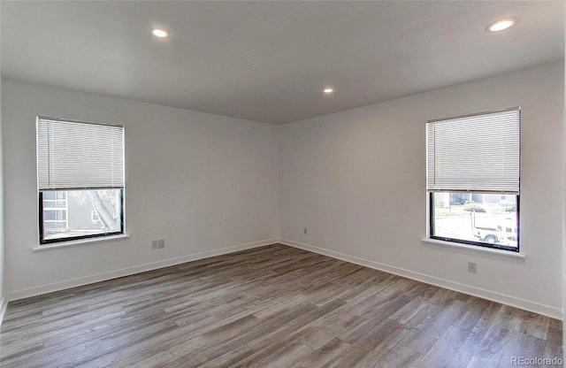 empty room featuring a wealth of natural light, baseboards, recessed lighting, and wood finished floors