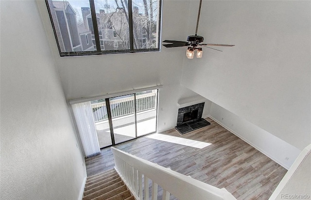 unfurnished living room featuring a high ceiling, a fireplace, wood finished floors, a ceiling fan, and baseboards