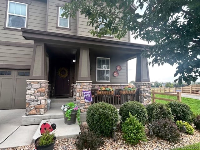 view of exterior entry featuring a garage, stone siding, and covered porch