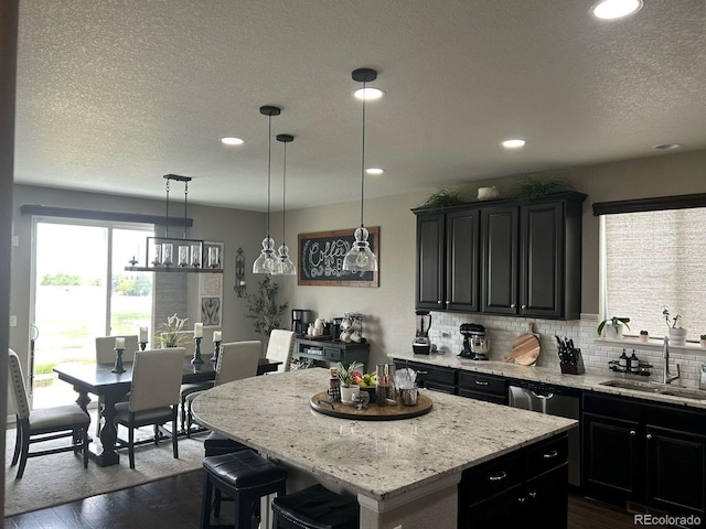 kitchen featuring dark cabinets, a kitchen island, a sink, backsplash, and dark wood finished floors