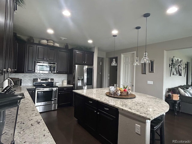 kitchen with tasteful backsplash, appliances with stainless steel finishes, hanging light fixtures, light stone counters, and a center island