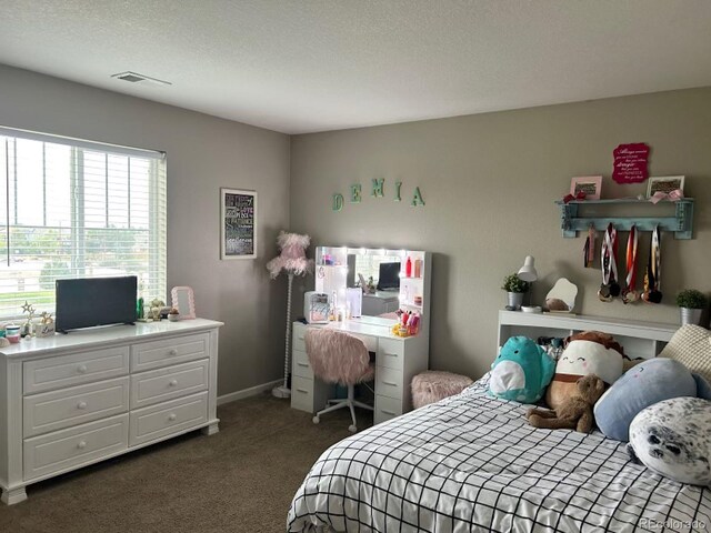 bedroom with a textured ceiling, dark colored carpet, visible vents, and baseboards