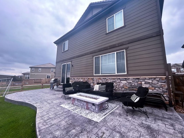 back of house with an outdoor living space with a fire pit, stone siding, a patio area, and fence