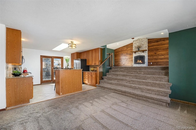 kitchen with open floor plan, light carpet, a kitchen island, a textured ceiling, and vaulted ceiling with skylight