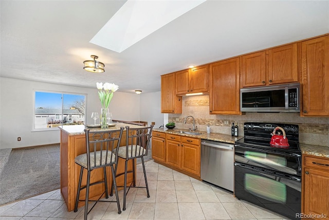 kitchen featuring stainless steel appliances, a sink, backsplash, light stone countertops, and brown cabinetry