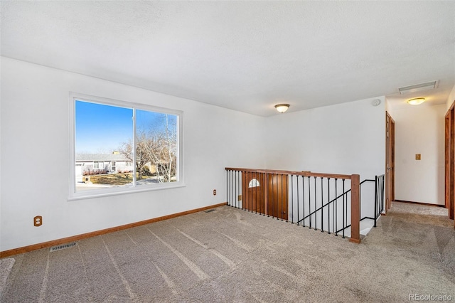 carpeted empty room featuring visible vents, a textured ceiling, and baseboards