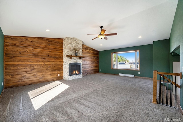 unfurnished living room featuring carpet, vaulted ceiling, wood walls, a fireplace, and a baseboard heating unit