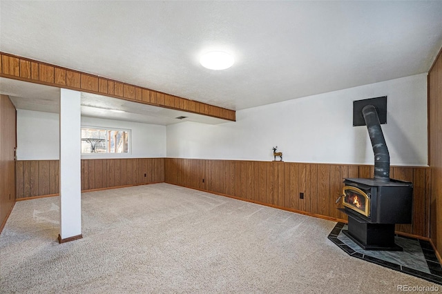 below grade area featuring a wood stove, carpet, wooden walls, and wainscoting