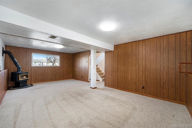 basement with carpet floors, wood walls, visible vents, stairs, and a wood stove