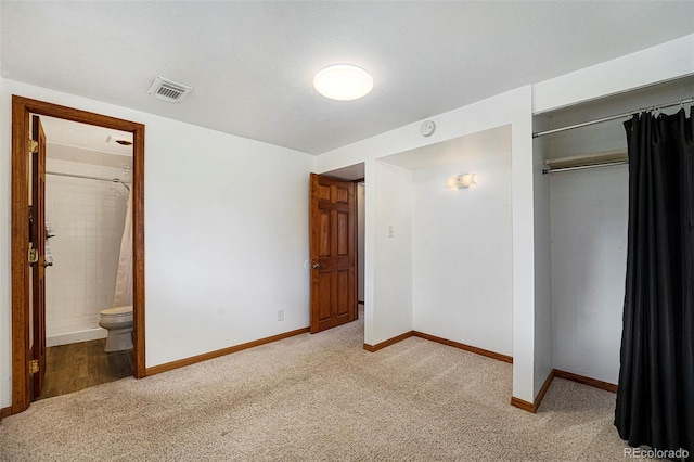 unfurnished bedroom featuring light carpet, visible vents, baseboards, a closet, and ensuite bath