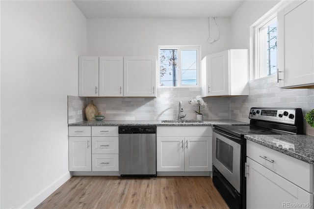 kitchen featuring sink, white cabinetry, dark stone countertops, stainless steel appliances, and light wood-type flooring