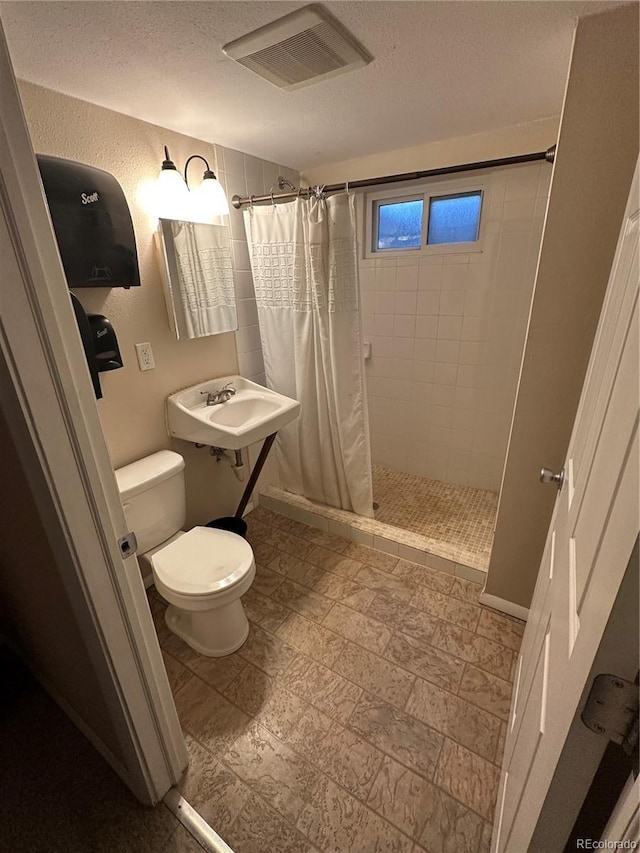 bathroom featuring a textured ceiling, toilet, curtained shower, and sink