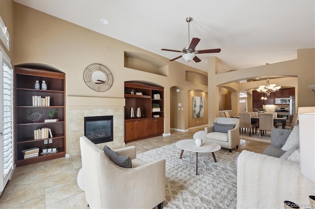 living area with arched walkways, baseboards, built in features, ceiling fan with notable chandelier, and a high end fireplace