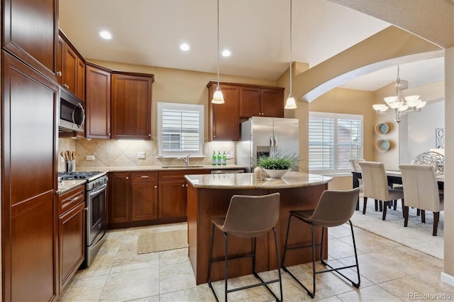 kitchen featuring arched walkways, a sink, an inviting chandelier, a kitchen island, and appliances with stainless steel finishes