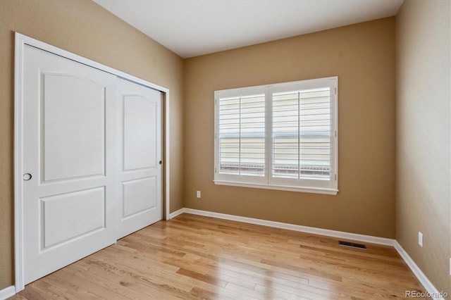 unfurnished bedroom featuring light wood-type flooring, baseboards, visible vents, and a closet