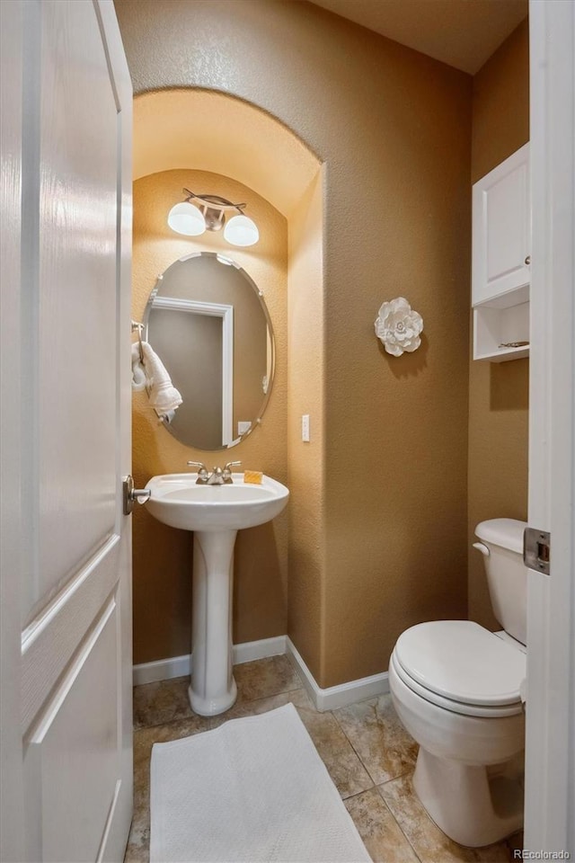 half bath with toilet, a textured wall, a sink, and baseboards
